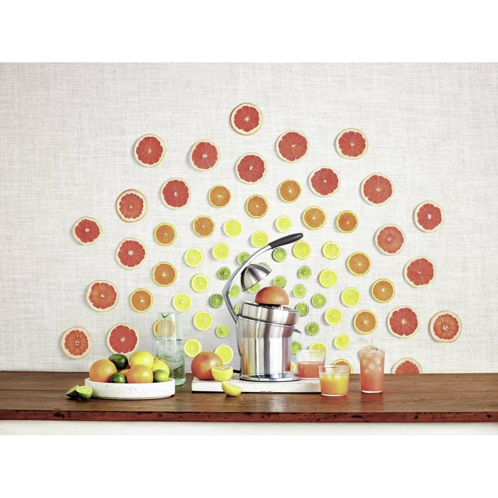 Tranches d'agrumes et presse-agrumes sur une table devant un mur à motif d'agrumes.