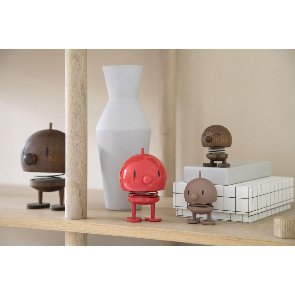 Quattro figure a molla su uno scaffale: rossa, marrone, legno e legno con faccia. Un vaso bianco dietro.