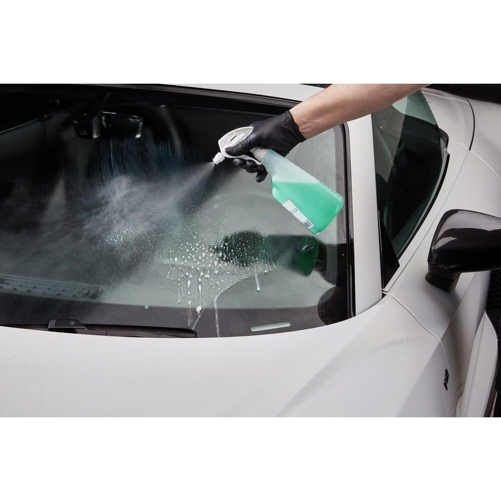 Un liquide vert est pulvérisé sur le pare-brise d'une voiture pour le nettoyer.