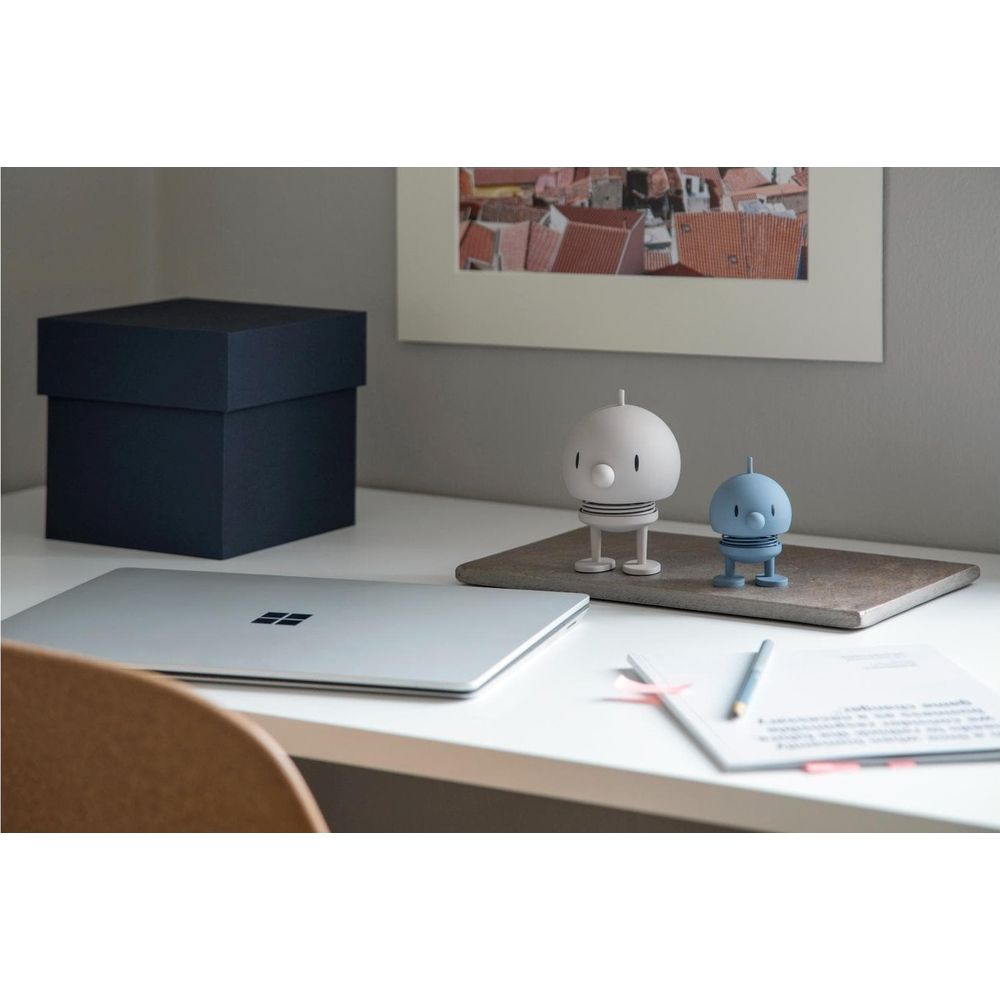 Una scrivania con laptop, scatola, due figure e un quadro sullo sfondo.