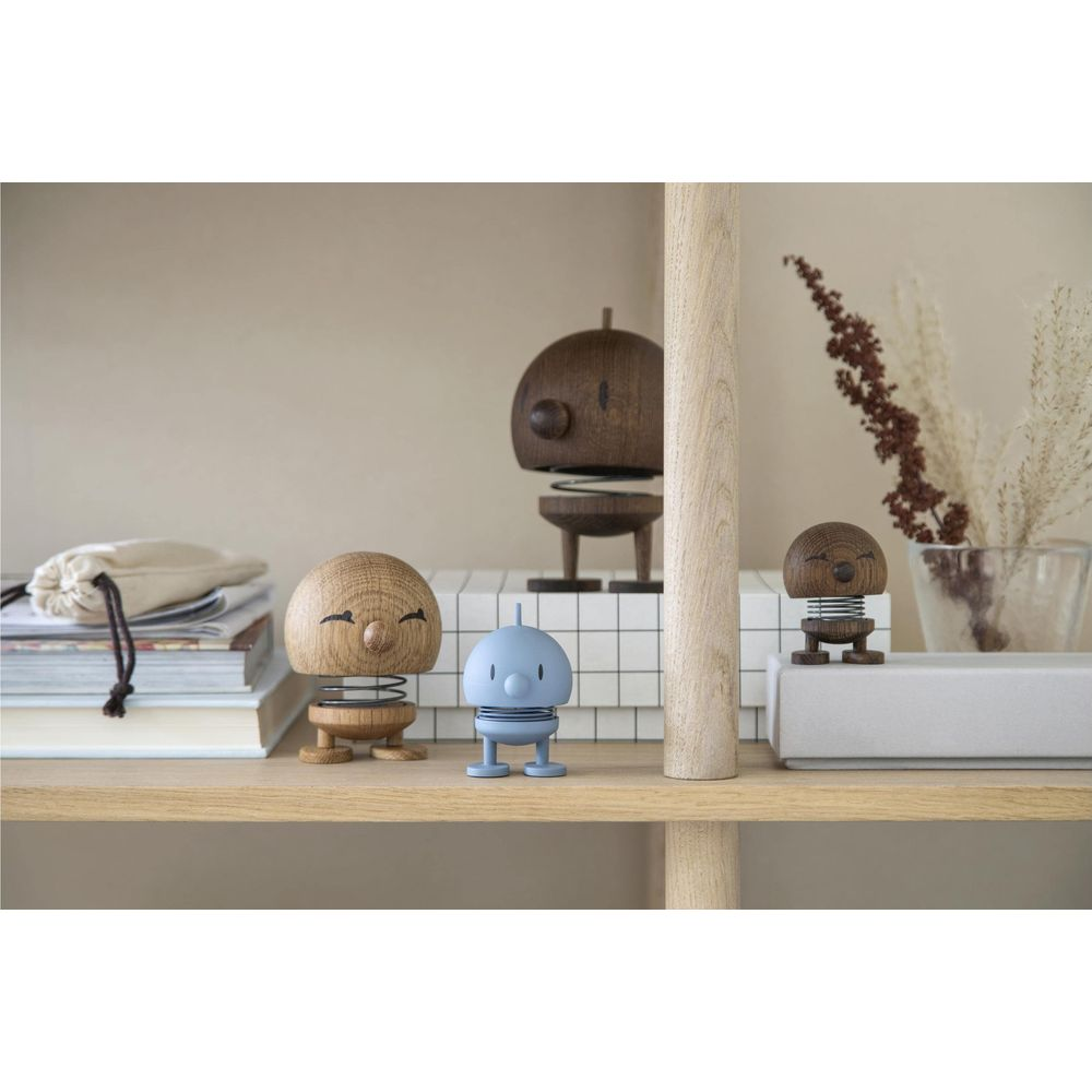 Tre piccole figure su uno scaffale: due di legno, una blu.