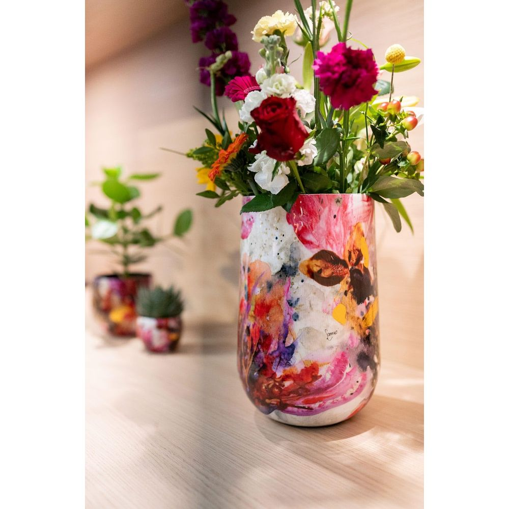 Ein bunter Blumenstrauß in einer abstrakten Vase steht auf einem Holztisch.