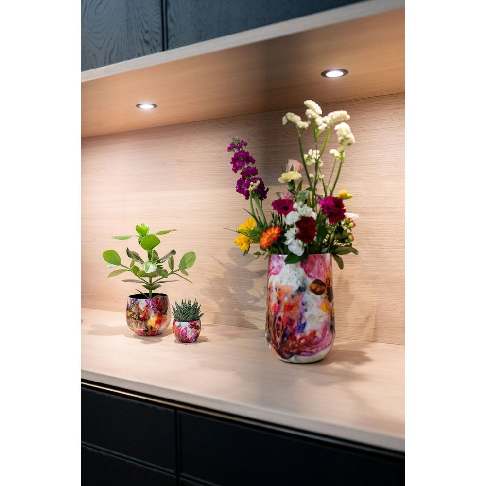Bunte Blumen in einer Vase und zwei Pflanzen auf einem Holzboden.