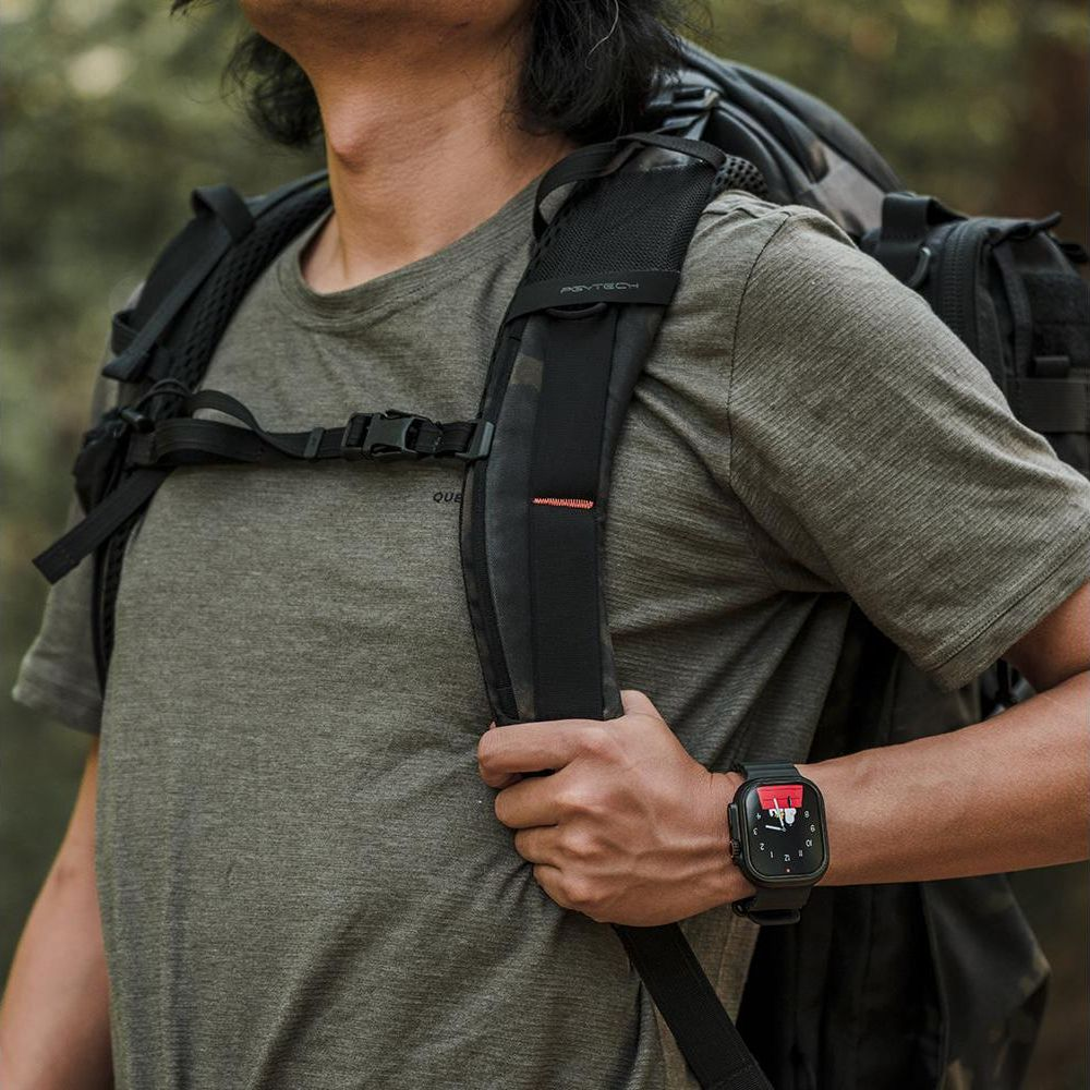 Homme avec sac à dos et montre connectée en zone boisée.