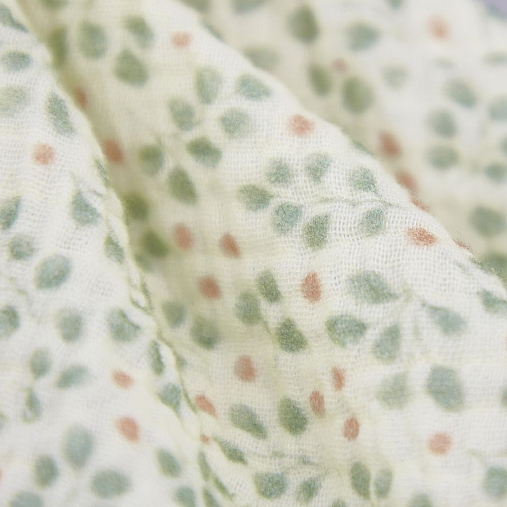 Tessuto beige chiaro con fantasia di foglie verdi e pois rosa.