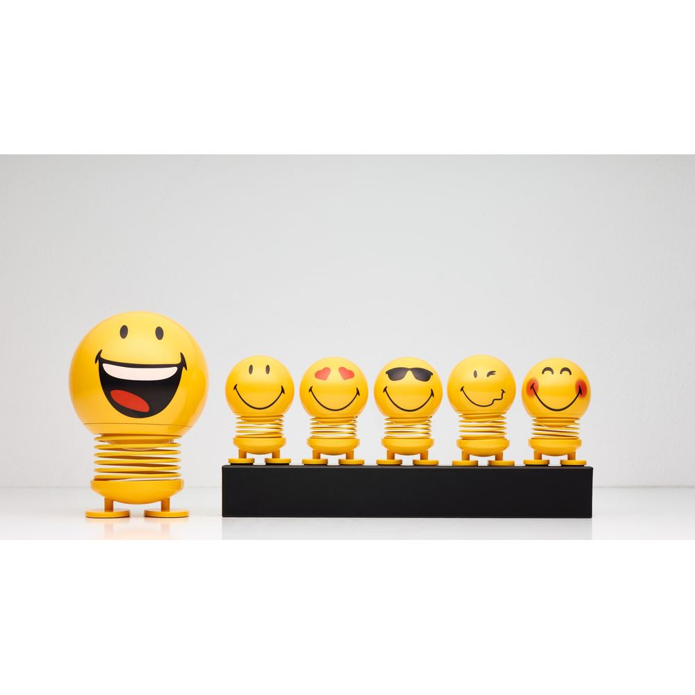 Sei pupazzi emoji gialli su supporto nero su sfondo bianco.