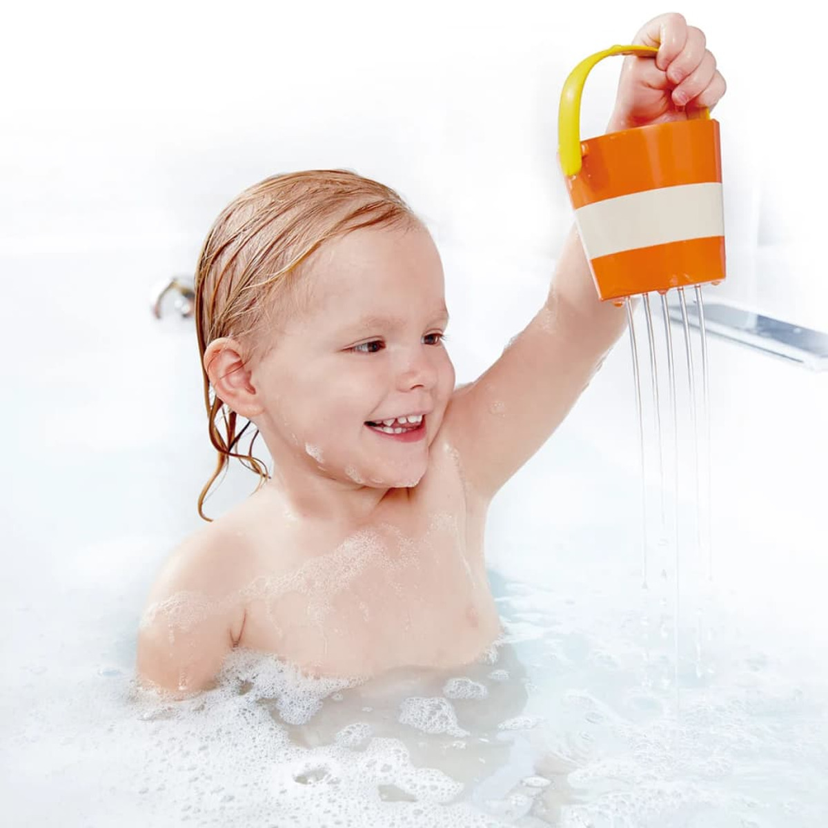 Un enfant souriant dans une baignoire joue avec un seau qui goutte.