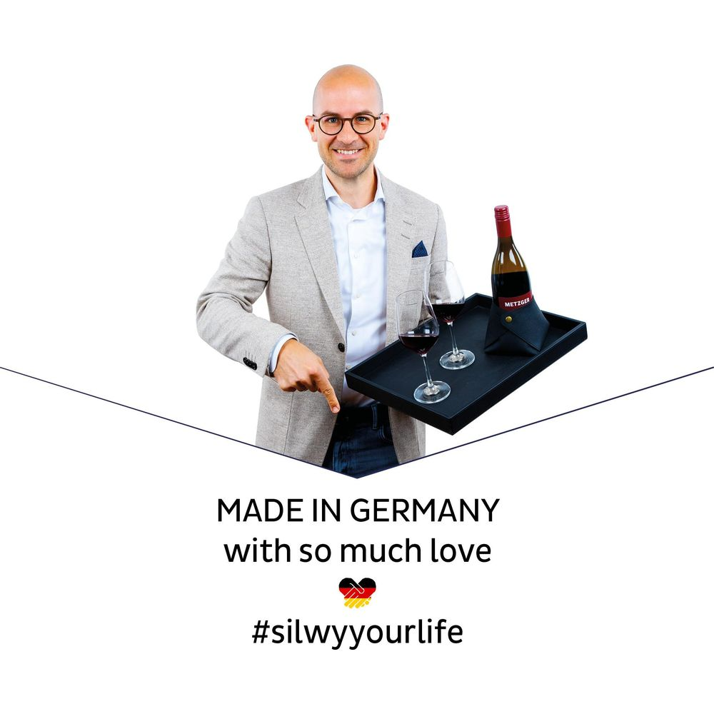 Ein Mann mit Brille zeigt auf ein Tablett mit Wein, Gläsern und einer Flasche.