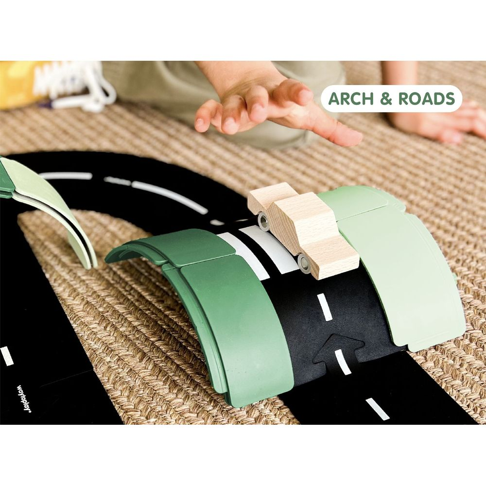 Mains d'un enfant près de voitures jouets en bois sur une route noire avec des ponts en arc verts sur un tapis tressé.