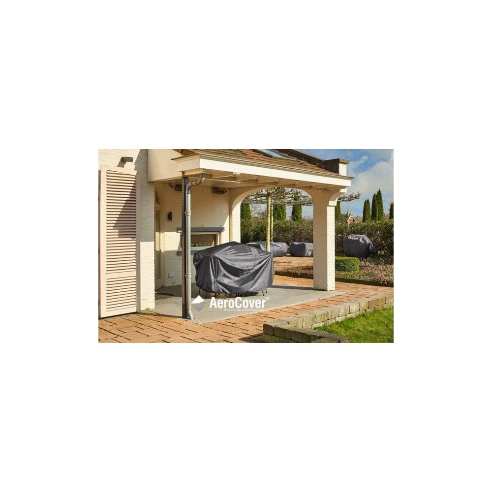 Ein grauer Grill unter einer Abdeckung steht auf einer Terrasse.