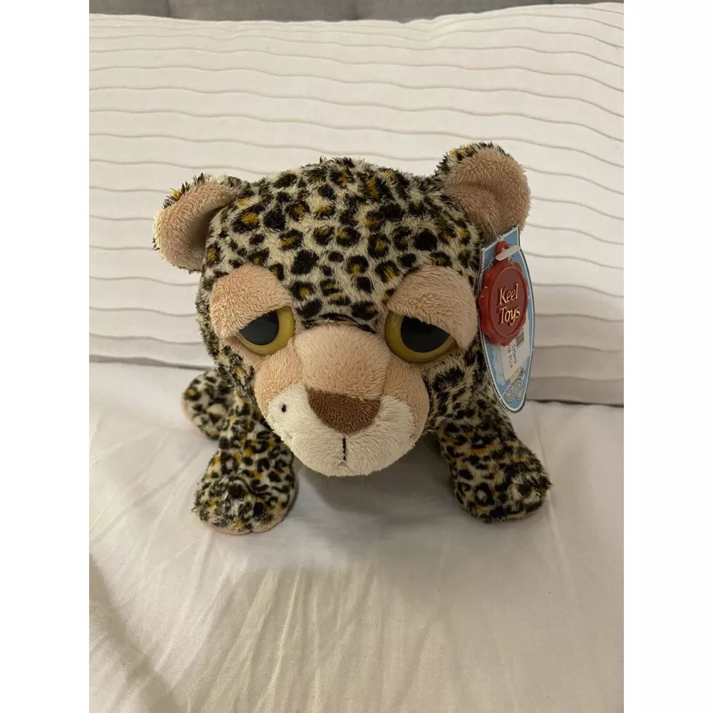 Un leopardo di peluche con occhi grandi e macchie giace su un cuscino a righe.