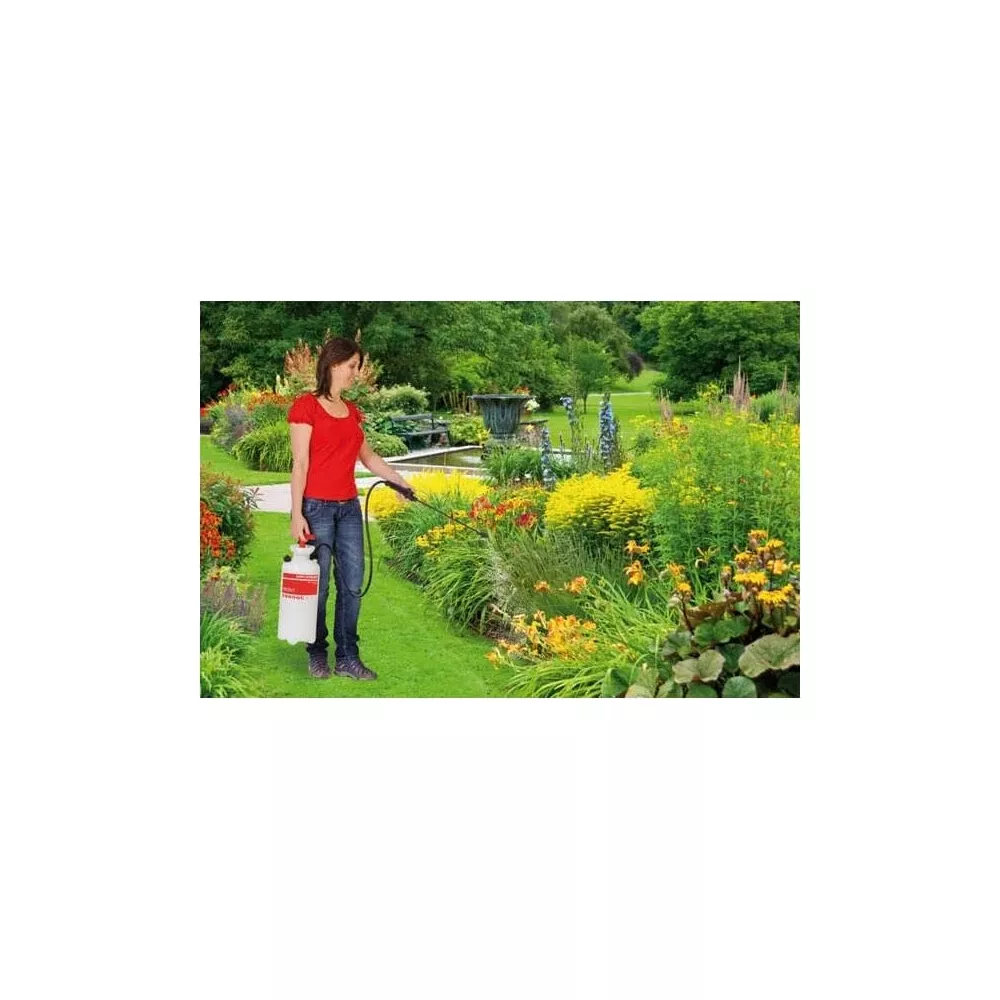 Eine Frau in Rot sprüht mit einem Gartensprühgerät in einer blühenden Blumenrabatte.