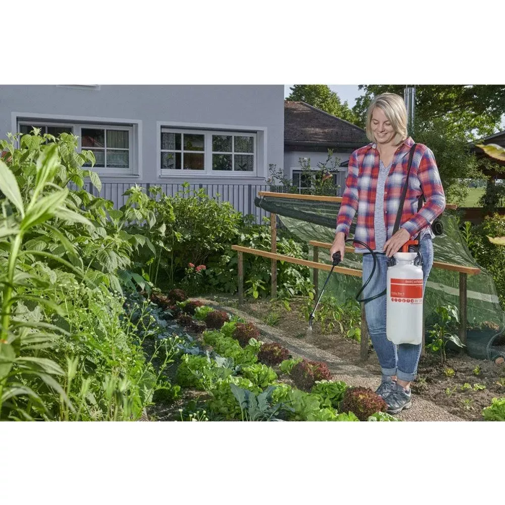 Frau sprüht mit Gartenspritze in einem Gemüsegarten mit Salatbeeten.