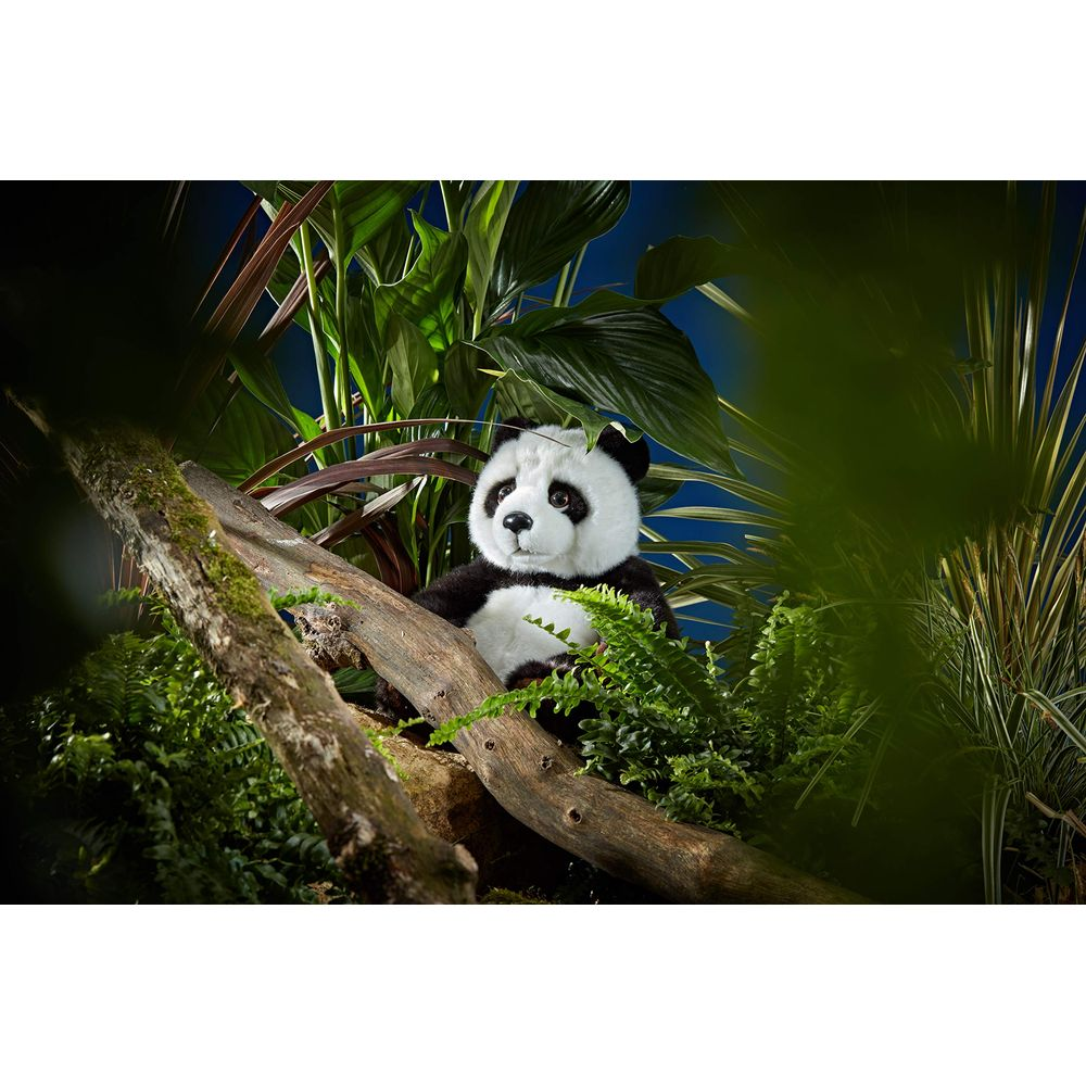 Un panda di peluche siede su un ramo in mezzo a fogliame lussureggiante e piante.