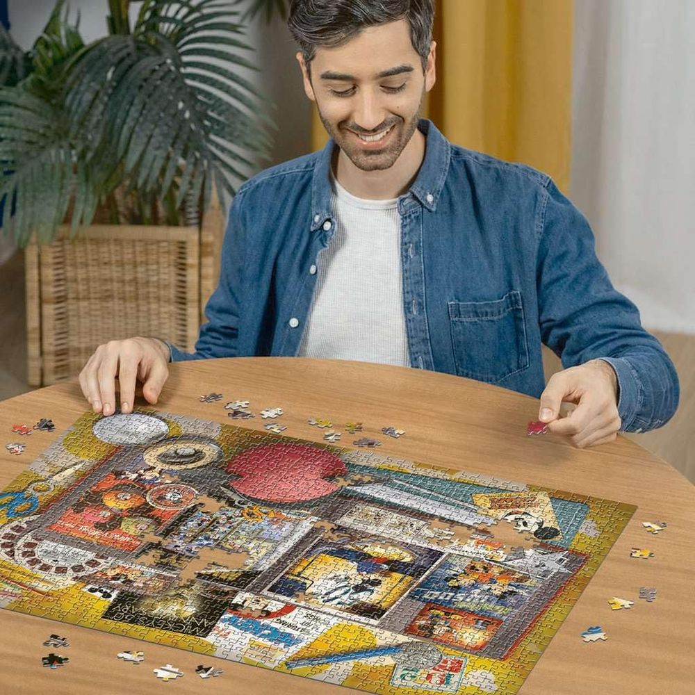 Mann im Jeanshemd setzt buntes Puzzle auf Holztisch zusammen. Im Hintergrund eine Pflanze.