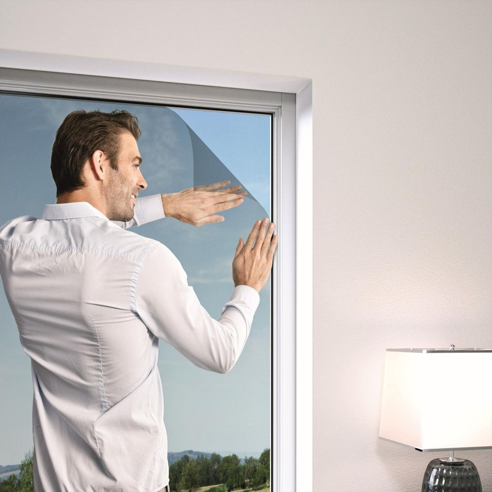 Mann klebt eine Tönungsfolie auf ein Fenster. Draußen ist es sonnig.