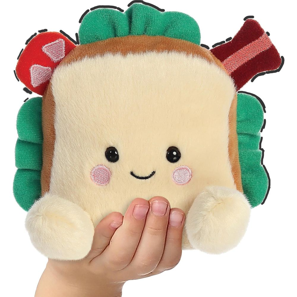 Un peluche a forma di panino con una faccia sorridente è tenuto dalla mano di un bambino.
