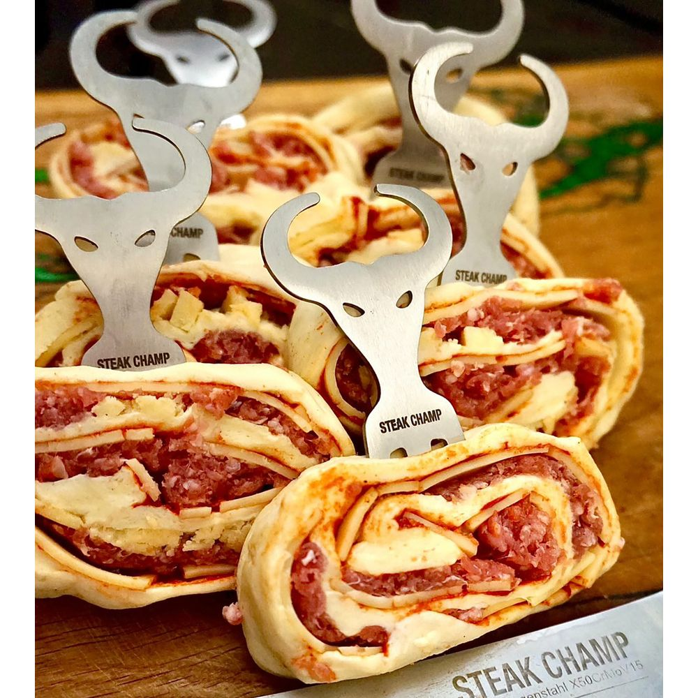 Fleischrolle mit Käse, mit Bullenköpfen dekoriert, auf Holzbrett.