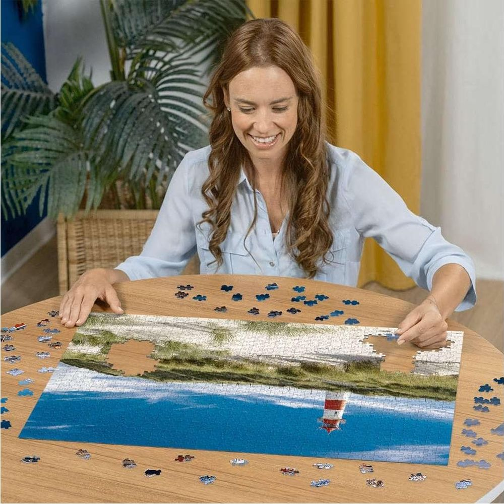 Frau setzt ein Puzzle eines Leuchtturms im blauen Wasser auf einem Holztisch zusammen.