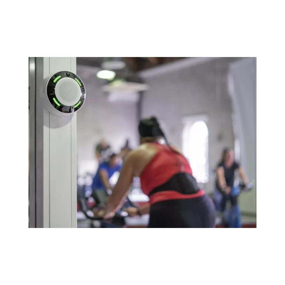 Ein weißer Sensor mit grünen Lichtern an einer Wand, im Hintergrund Radfahrer.
