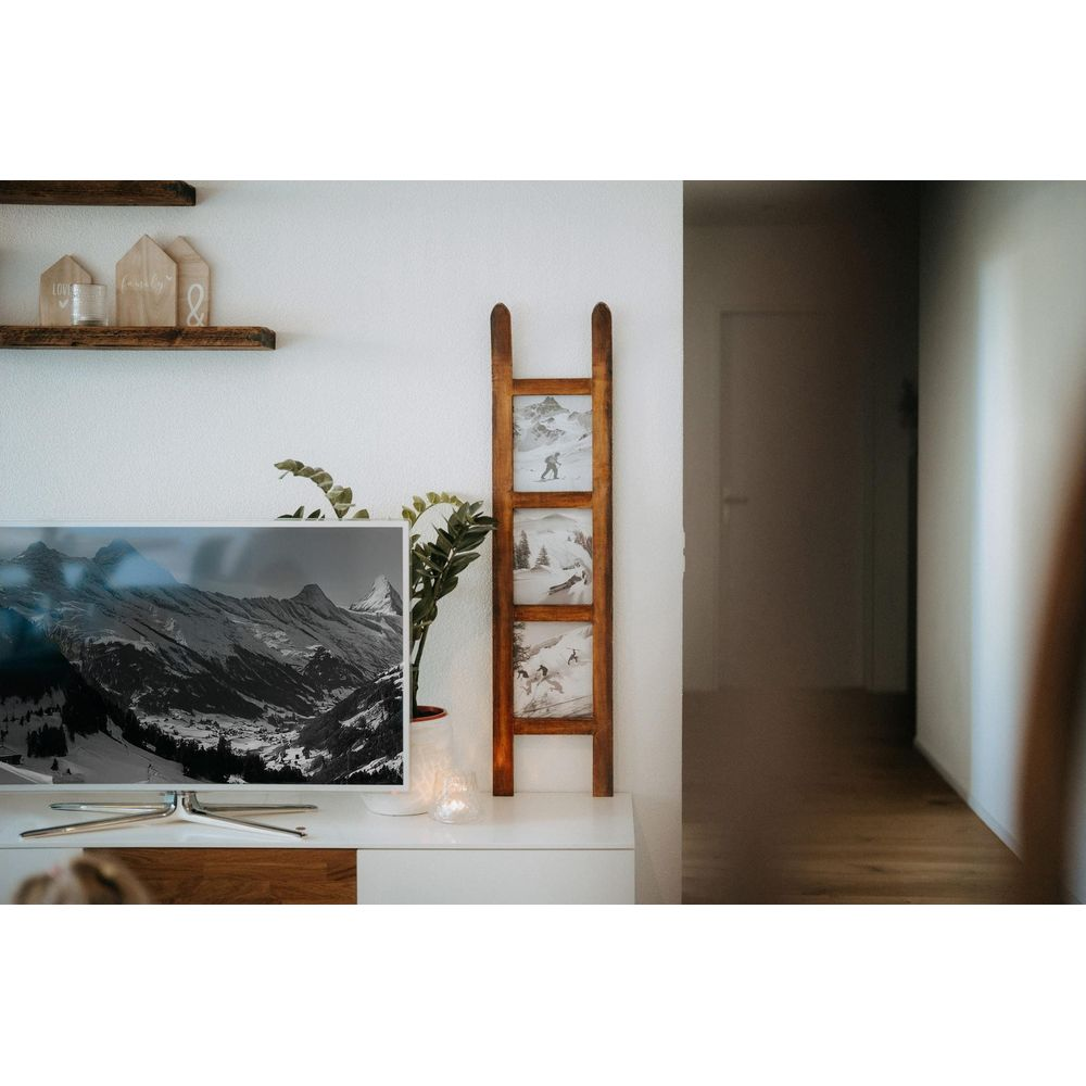 Une TV montre des montagnes. Devant, un cadre en bois avec des photos de skieurs.