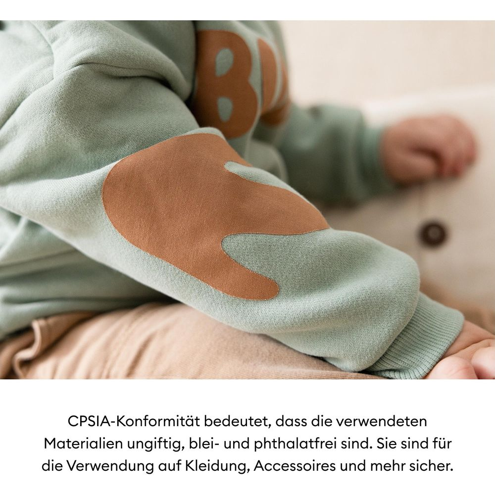 Ein hellgrüner Pullover mit braunen Ellbogenflicken und einem großen "B"-Aufdruck.