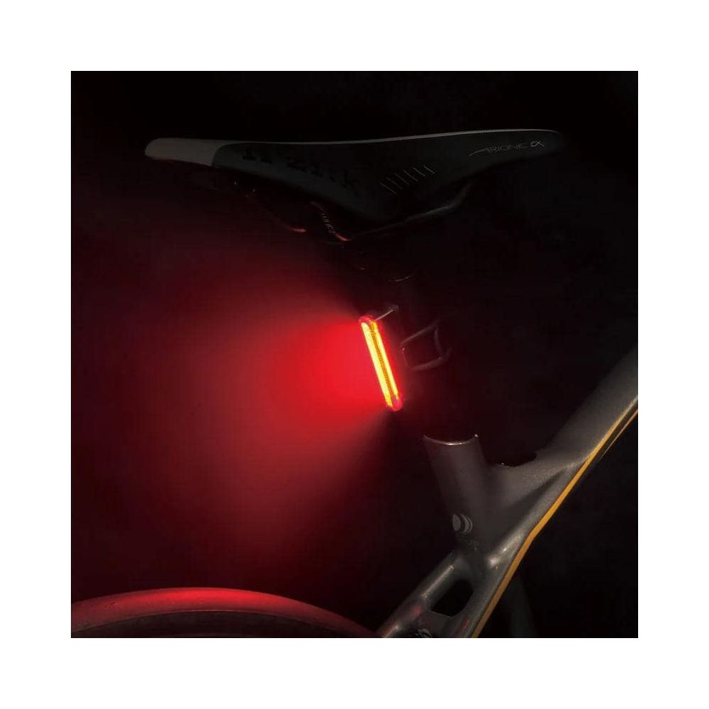 Ein rotes Fahrradrücklicht leuchtet hinter dem Sattel eines dunklen Fahrradrahmens.