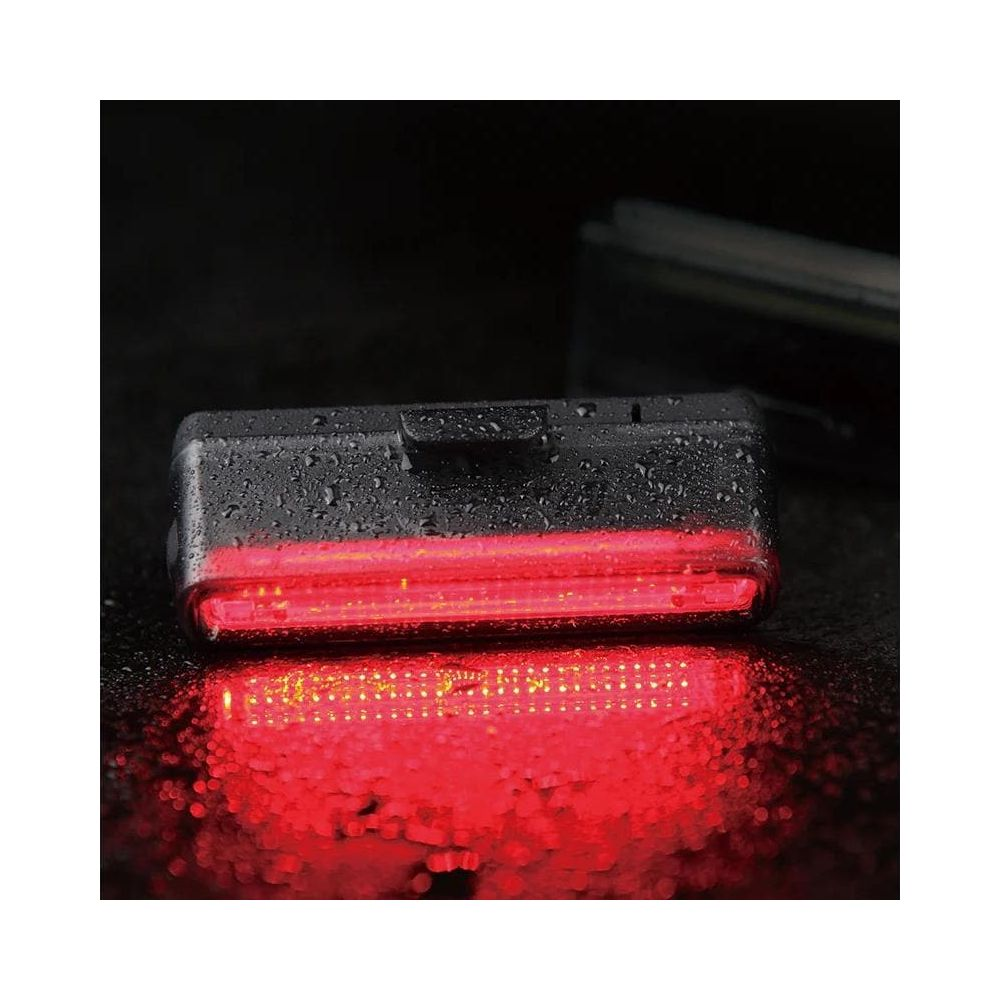 Rotes Fahrradrücklicht mit Wassertropfen auf schwarzem Untergrund.