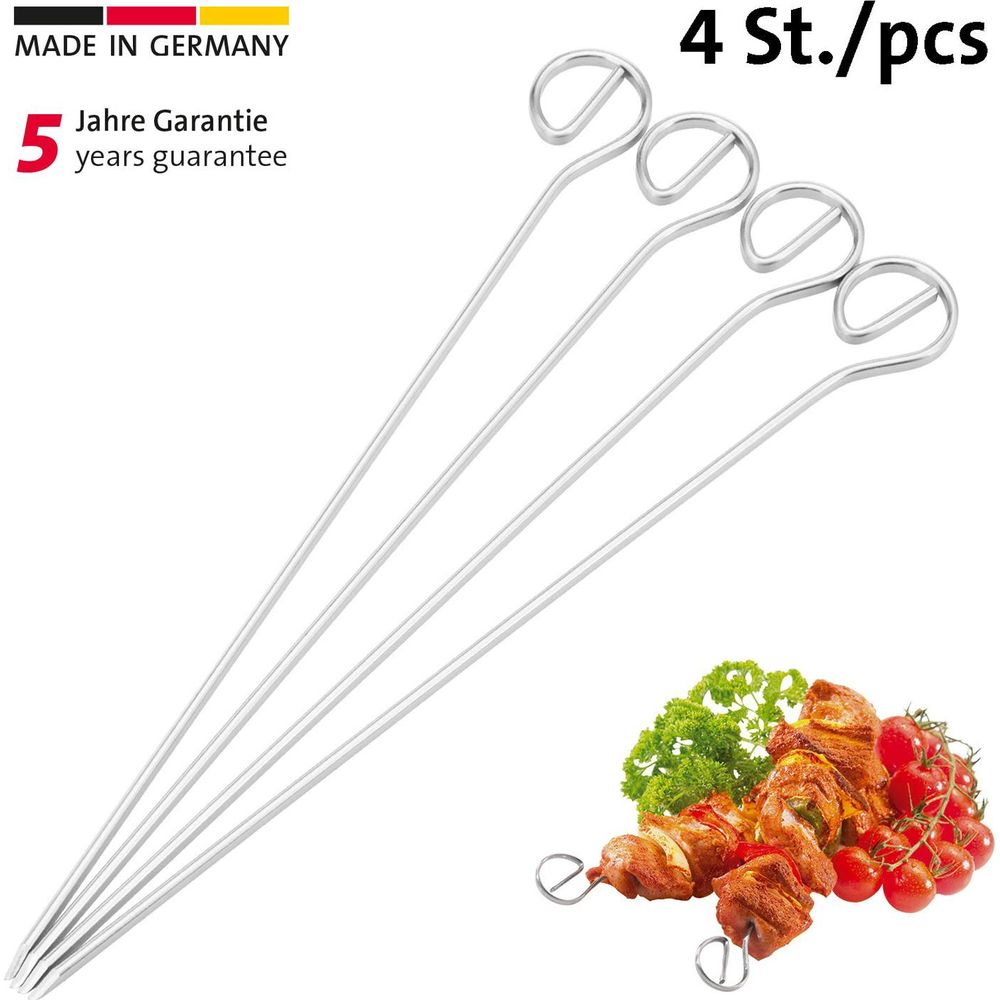 Quattro spiedini metallici con manico ad anello, accanto a carne grigliata e pomodorini.