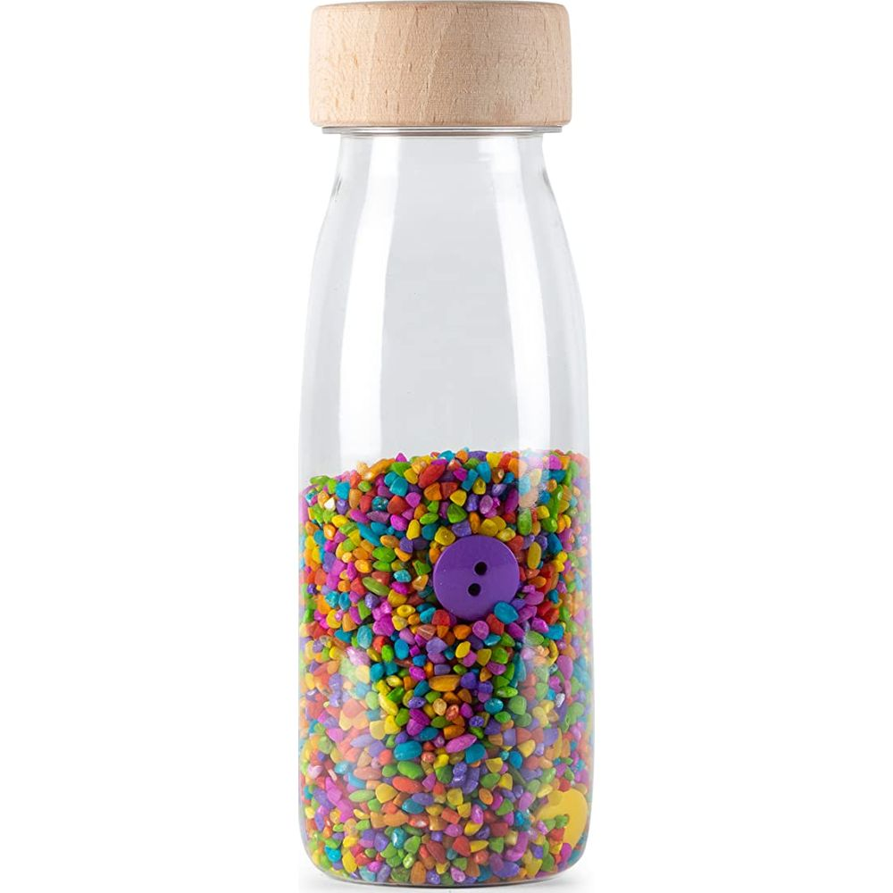 Eine Glasflasche mit Holzboden, gefüllt mit bunten Kieselsteinen und einem lila Knopf.