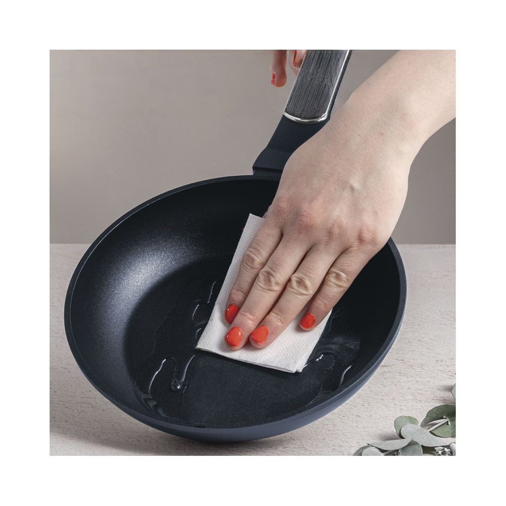 Une main aux ongles rouges essuie de l'huile dans une poêle avec une serviette en papier.