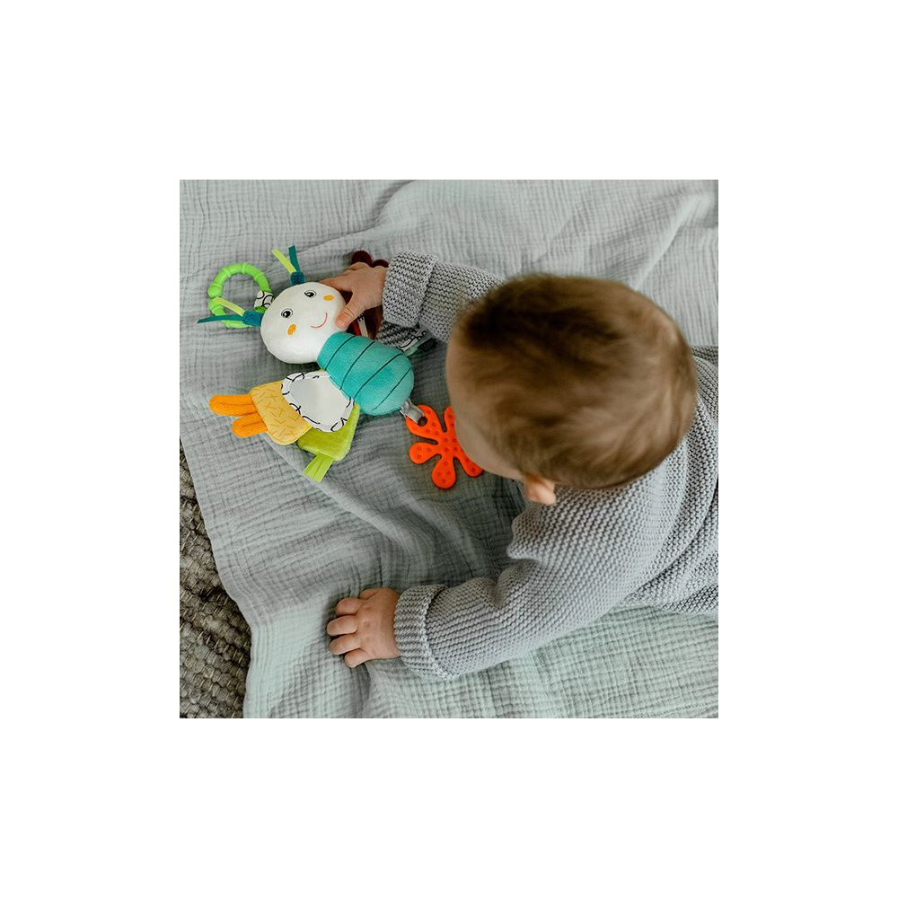 Un bébé en pull gris joue avec un jouet en peluche coloré sur une couverture grise.