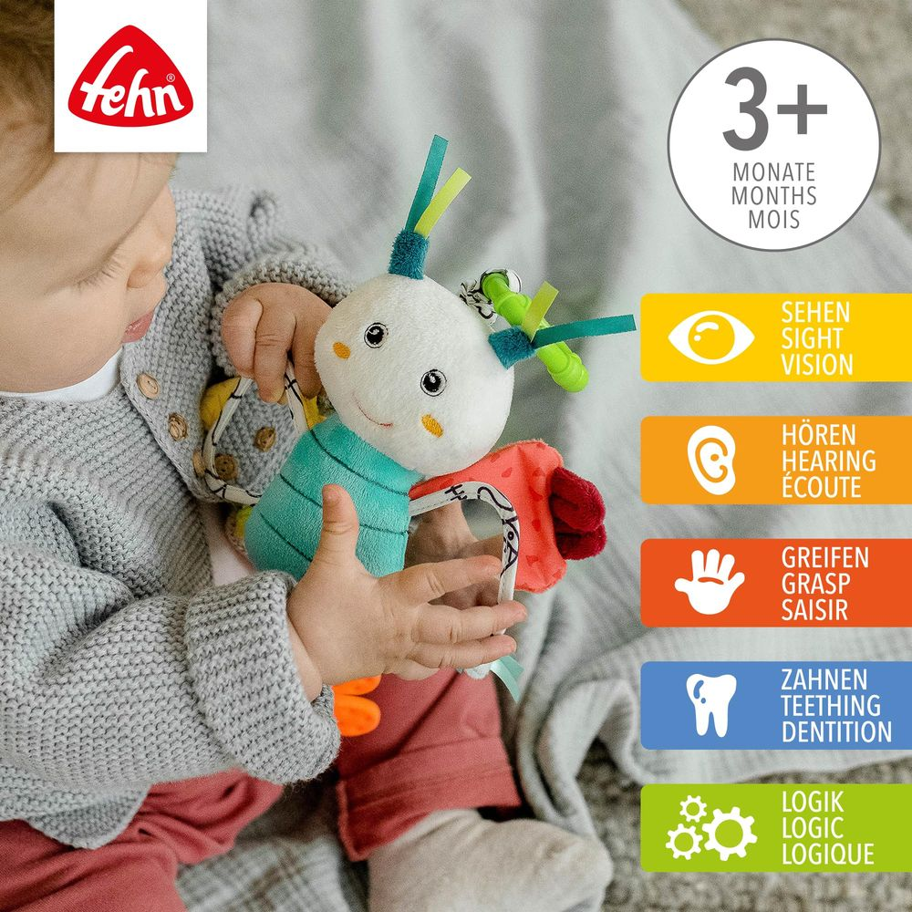 Un bébé tient un jouet en peluche coloré aux fonctions variées. Icônes montrent vue, ouïe, prise et poussée dentaire.