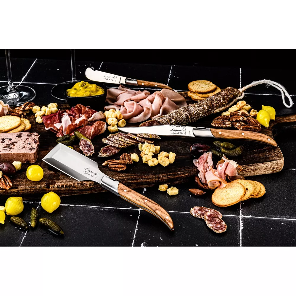 Wurstwarenplatte mit Käse, Brot, Früchten und Besteck auf schwarzem Untergrund.