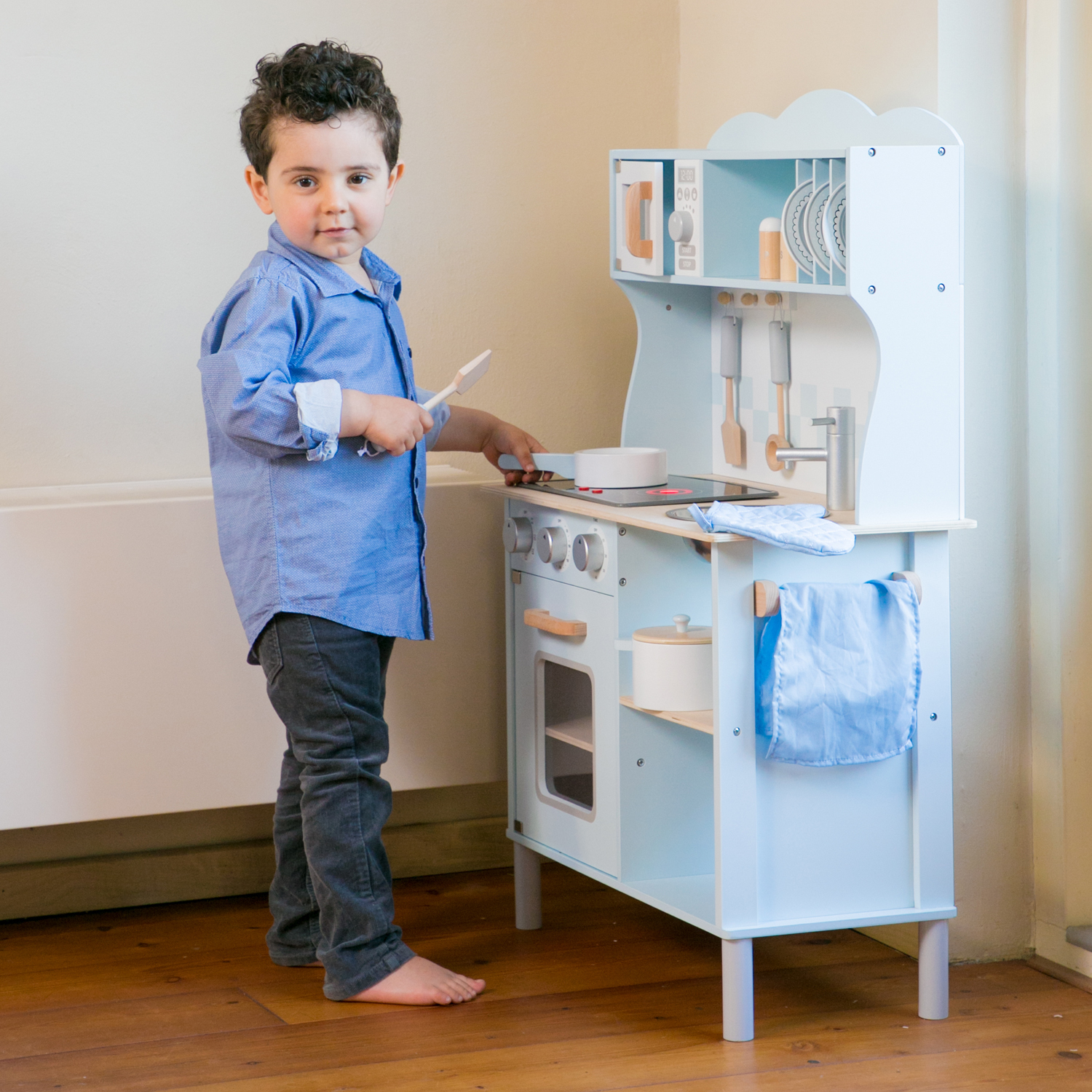 Un bambino con una camicia blu gioca con una cucina giocattolo azzurra.