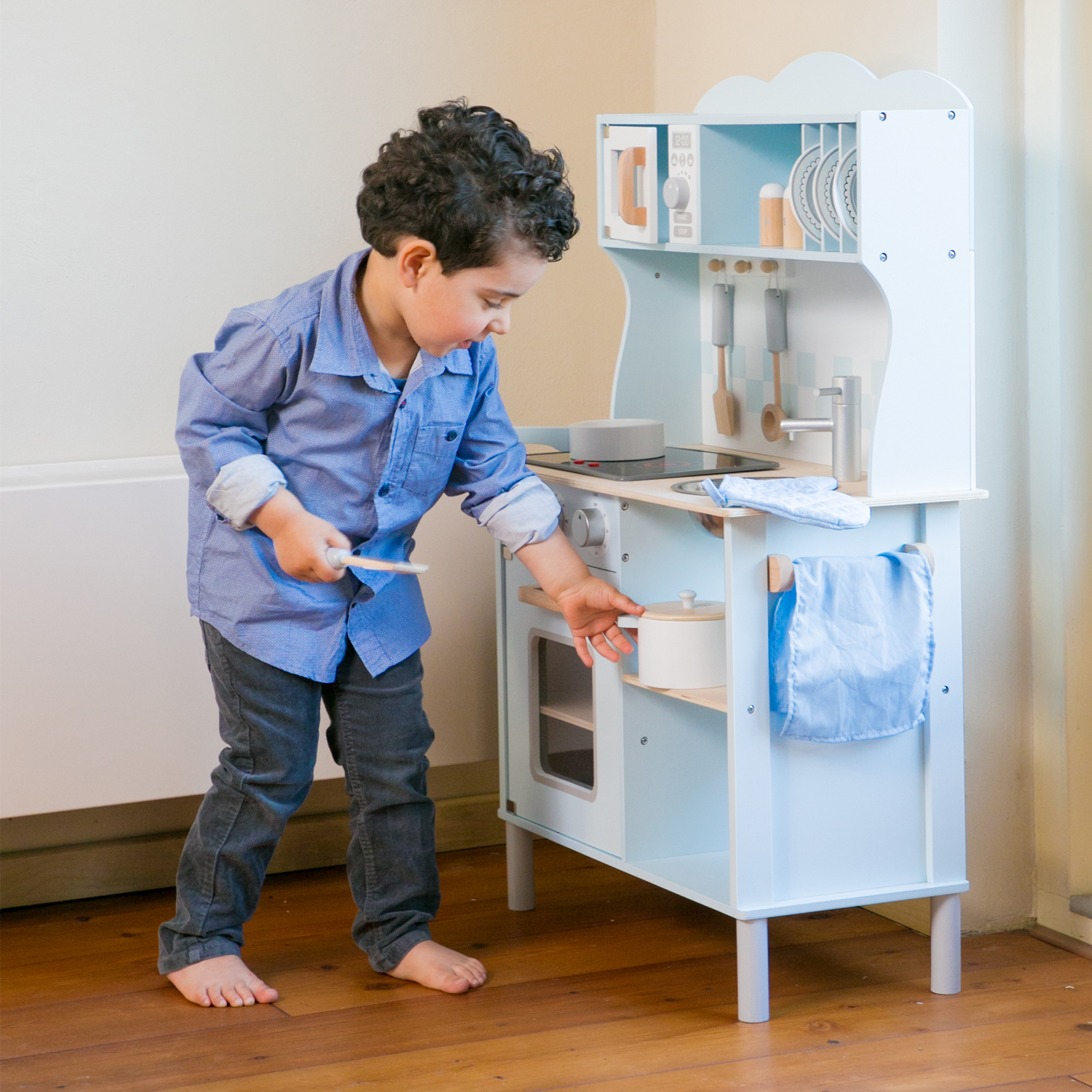 Un bambino con una camicia blu gioca con una cucina giocattolo di legno.