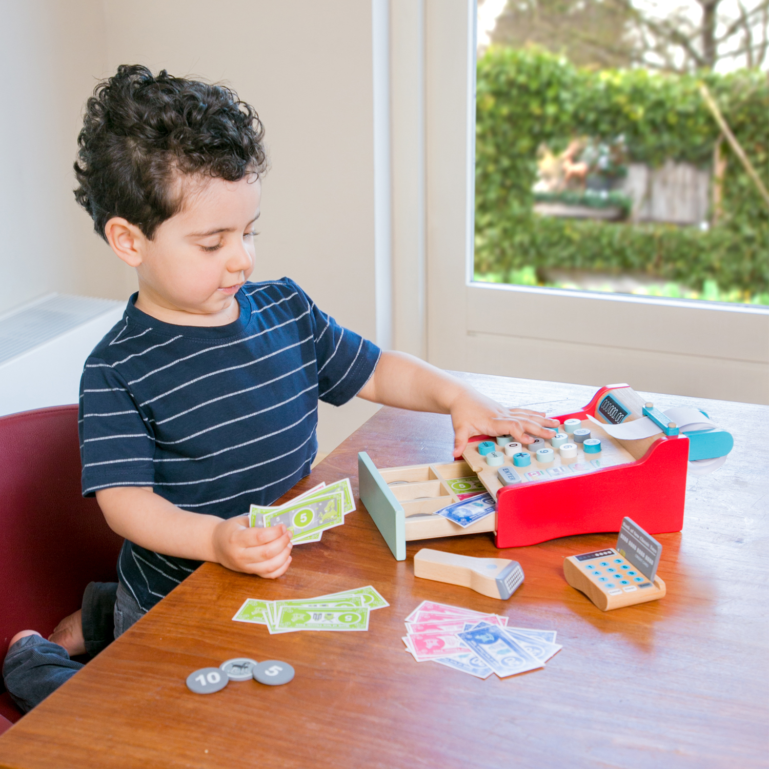 Ein kleiner Junge spielt mit einer hölzernen Registrierkasse und Spielgeld.