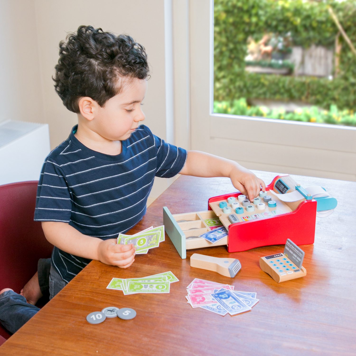 Ein Junge spielt mit einer hölzernen Spielzeugkasse und Spielgeld.