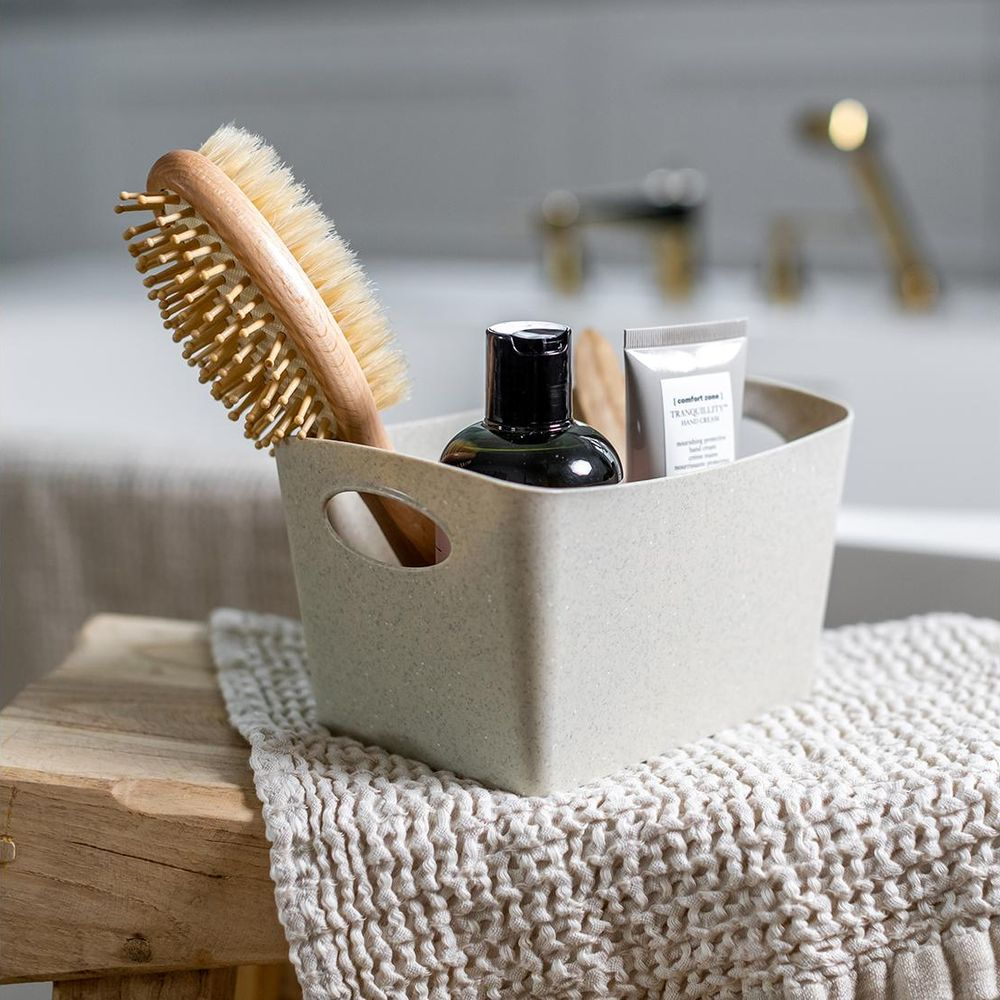 Ein heller Behälter mit Haarbürste, dunkler Flasche und Handcreme.