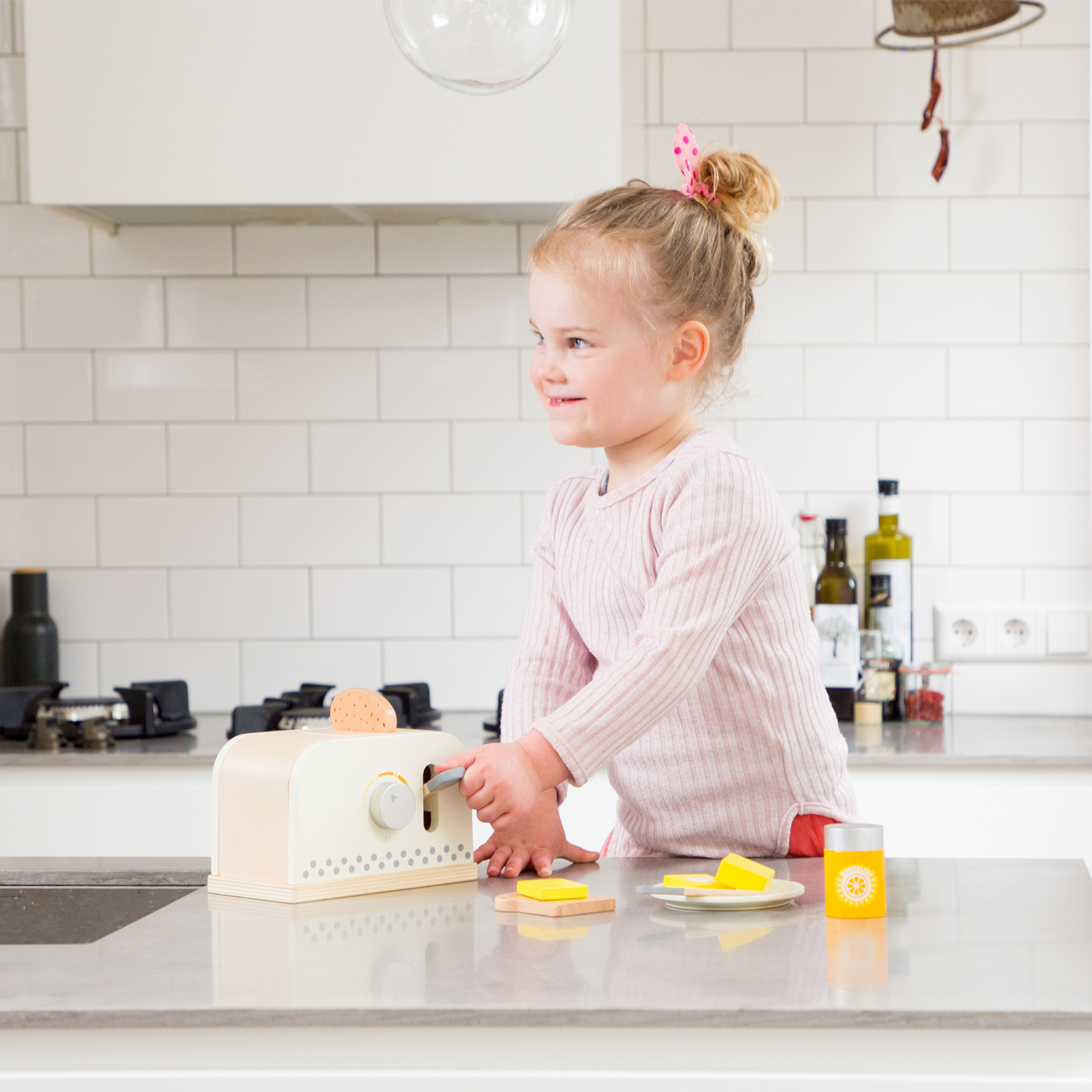 Una bambina in maglia rosa gioca con un tostapane giocattolo in cucina.
