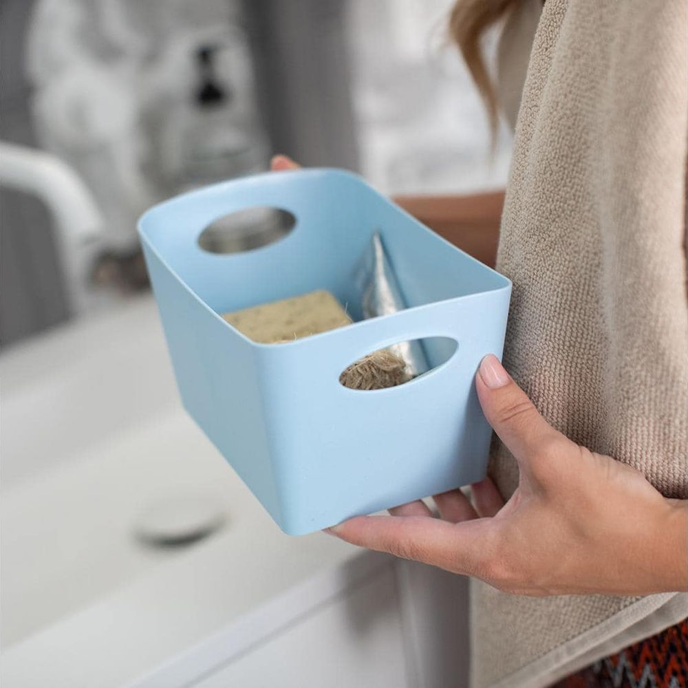 Ein hellblaues Körbchen mit Schwamm und Schnur wird über einem Waschbecken gehalten.