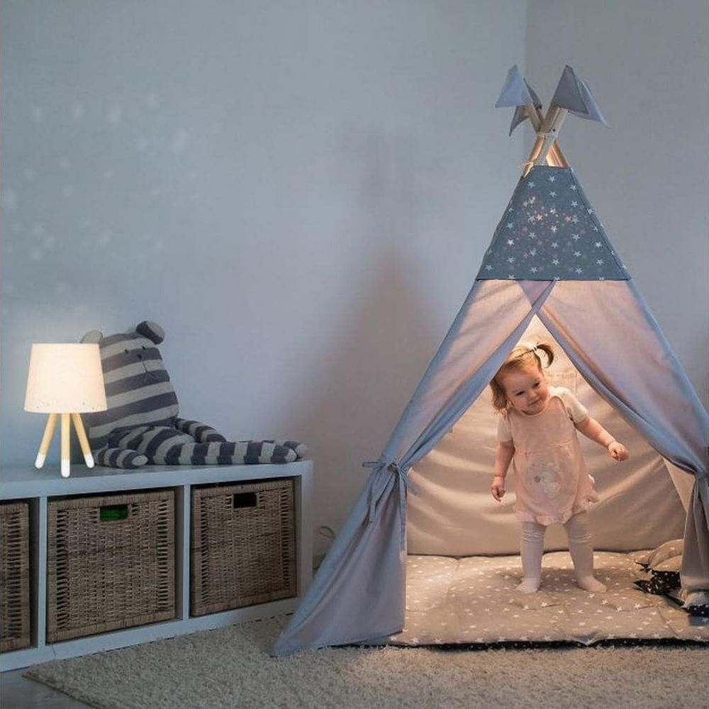 Ein kleines Mädchen steht in einem Sternen-Tipi. Ein Teddy sitzt neben einer Lampe.