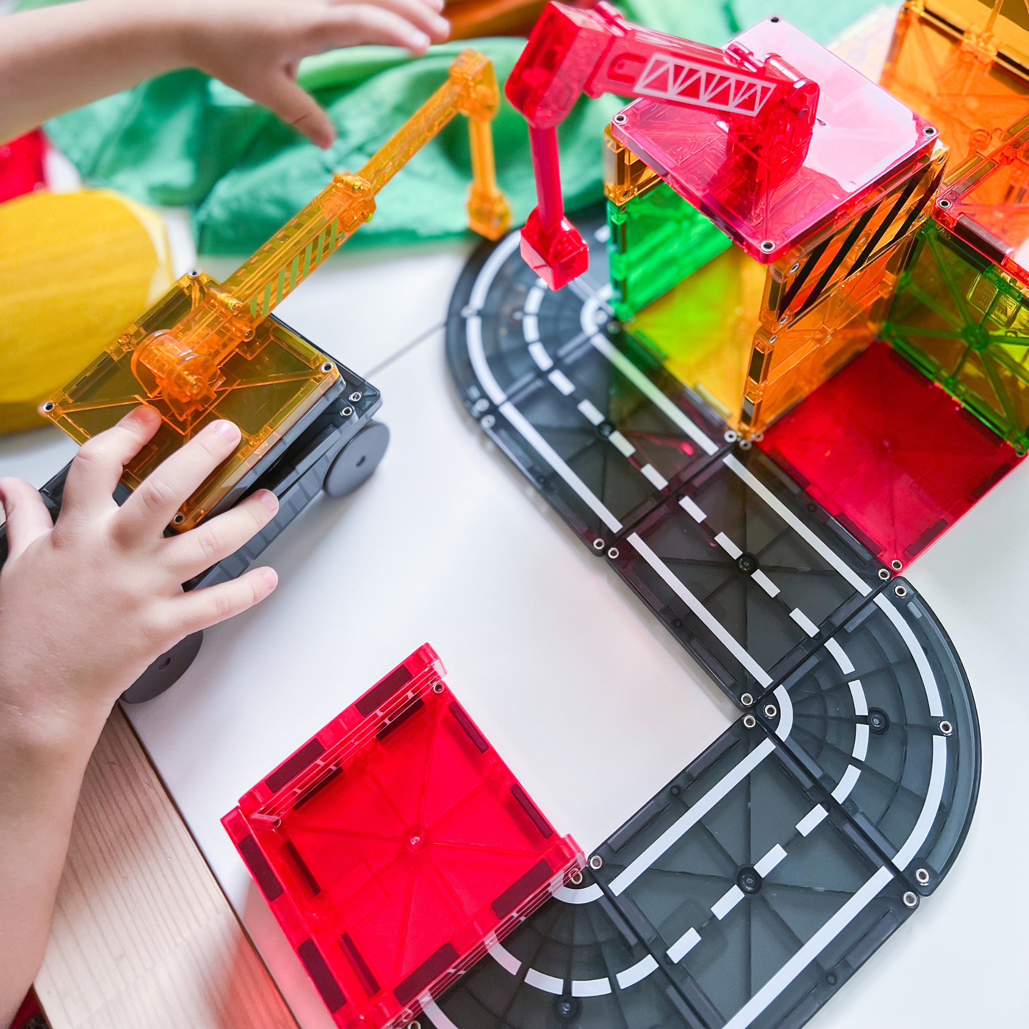Kinder bauen mit bunten Bausteinen und Kranspielzeug eine Rennstrecke.