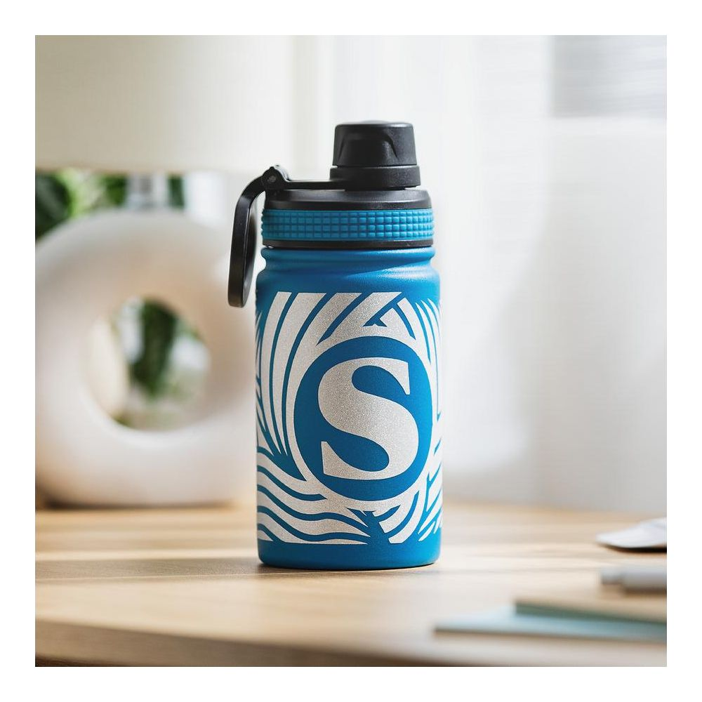Eine blaue Wasserflasche mit weißem Muster und 'S'-Logo steht auf einem Tisch.