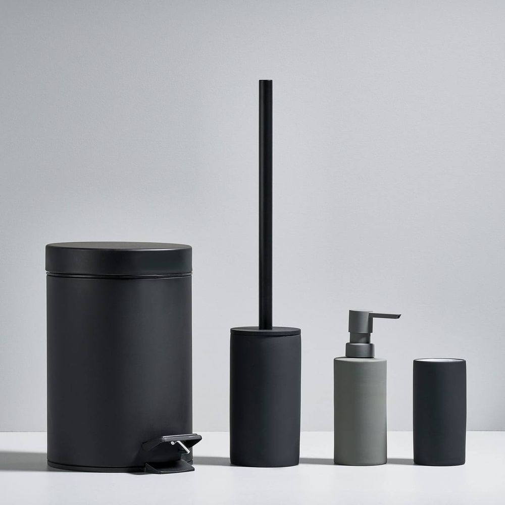 Ein schwarzer Mülleimer, eine schwarze Toilettenbürste, ein grauer Seifenspender und ein schwarzer Becher.