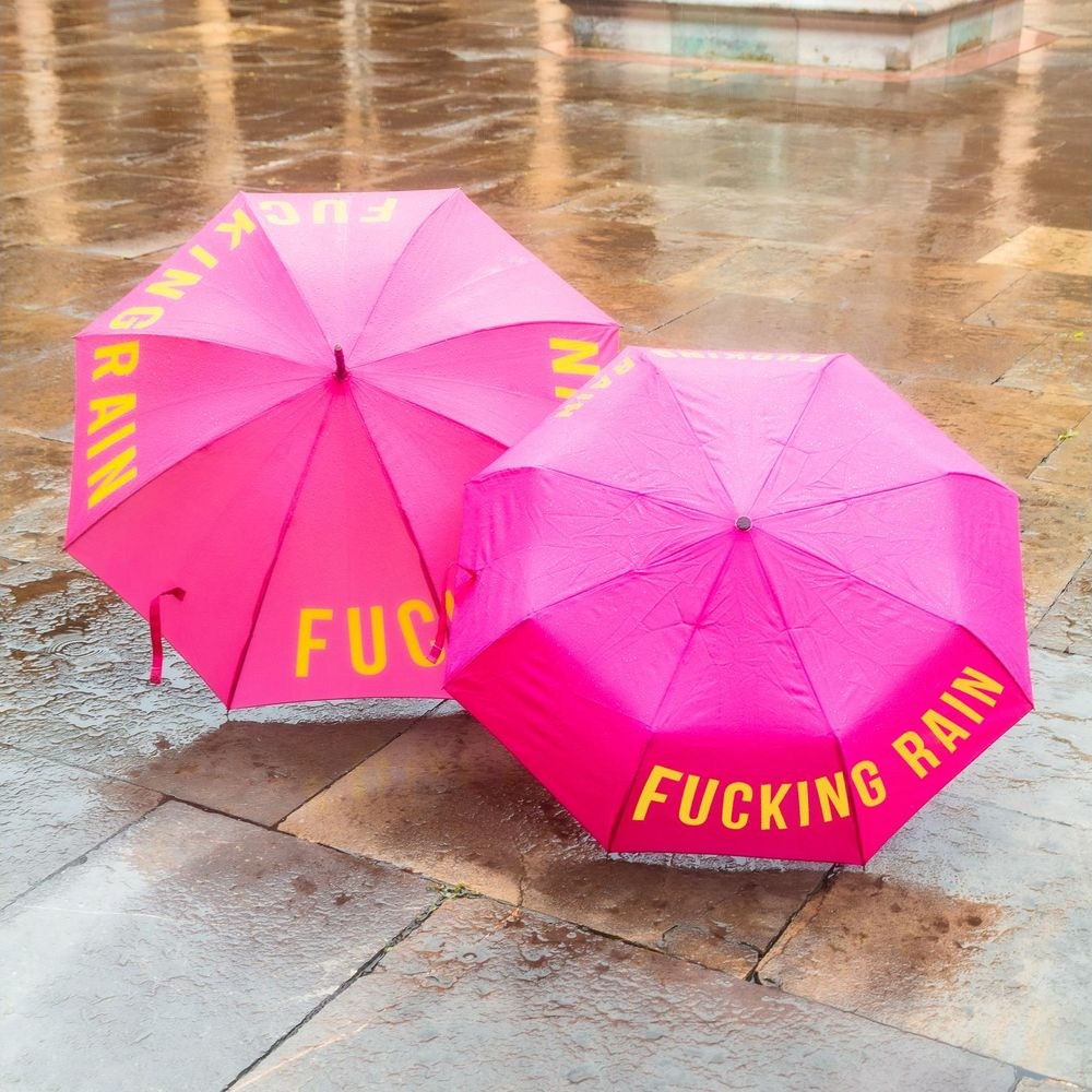 Zwei pinke Regenschirme mit gelbem Text liegen auf nassem Steinboden.