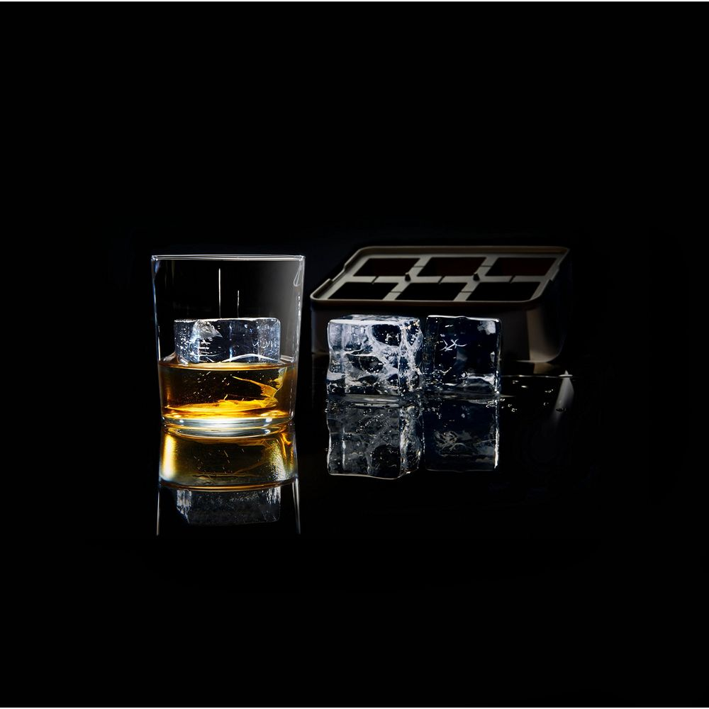 Un verre de whisky avec un glaçon, deux glaçons à côté et un bac à glaçons.