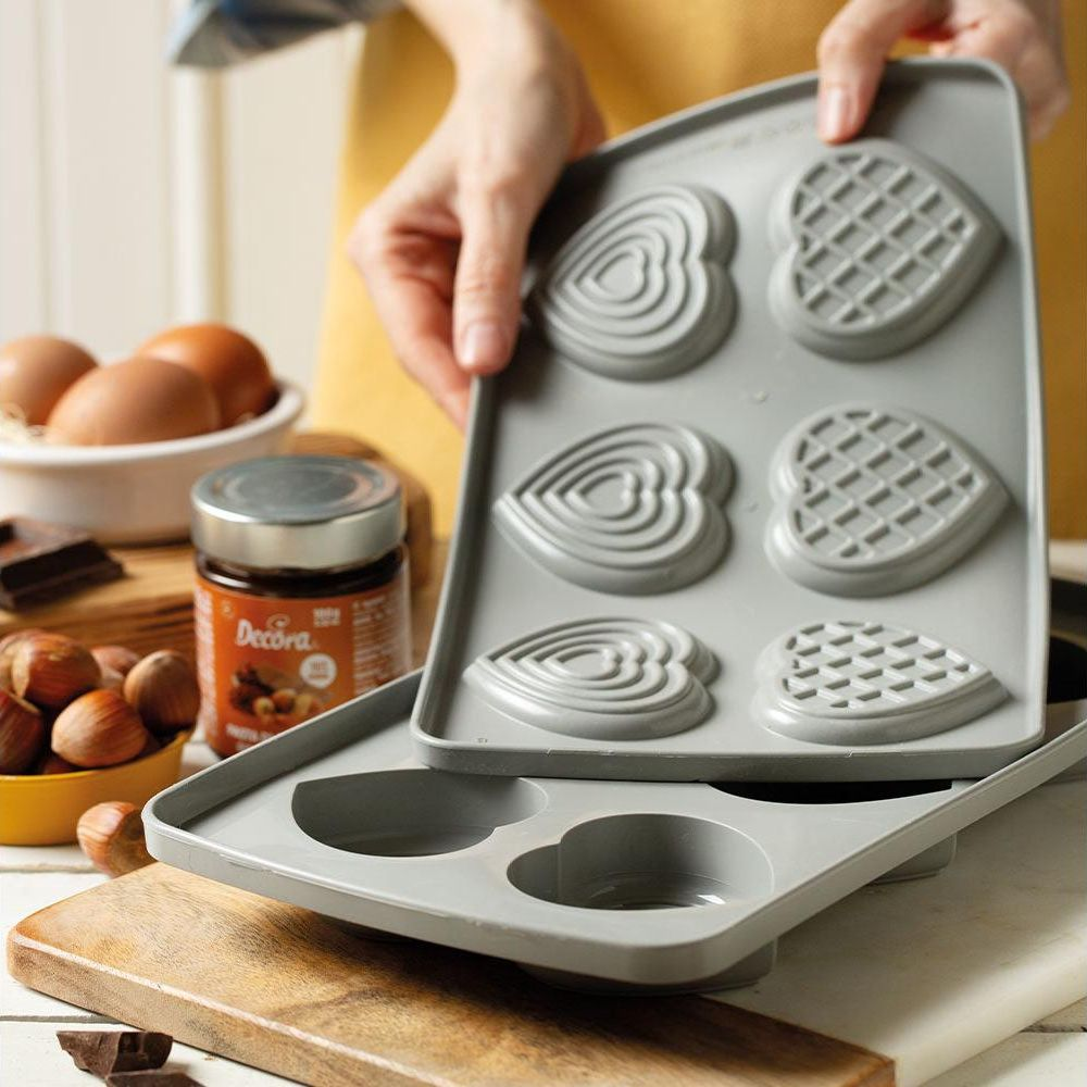 Graue Herz- und Waffelform mit Zutaten wie Eiern, Haselnüssen und Schokolade.