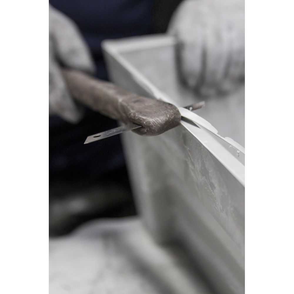 Person mit Handschuhen schneidet mit einem Messer auf einem Metallrahmen.