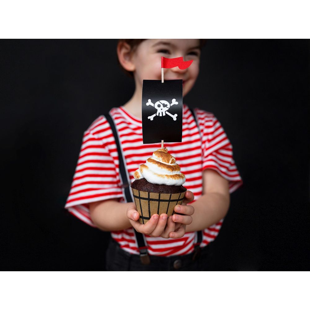 Ein Junge im Piratenkostüm hält einen Cupcake mit Totenkopf-Flagge.